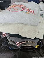 Stack of folded clothing showing multiple items including sweatshirts, jackets, and shirts in various colors and materials.