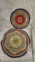 Two melamine plates, one dinner plate and one salad plate, laying on white cloth showing colorful floral and geometric patterns