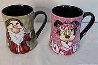 Front side view of Grumpy and Minnie Mouse Disney mugs, showing character designs and colors.