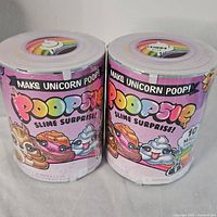 Front view of two sealed Poopsie Slime Surprise unicorn poop slime jars with colorful cartoon labels and branding.