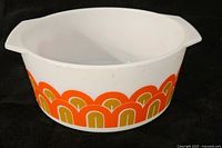 Side view of Pyrex casserole dish showing repeating fish scale pattern in orange and olive green on white milk glass