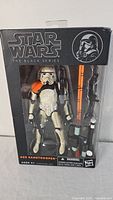 Front view of the boxed Star Wars The Black Series Sandtrooper figure with orange pauldron and weapon accessories visible.