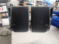 Front view of both black Aiwa speakers showing fabric covers, bass reflex ports, and gold logo.