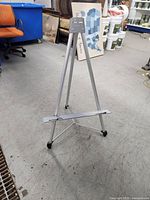 Front and side view of silver aluminum easel with adjustable height, tripod legs and black rubber feet.