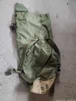 Olive green army duffel bag with canvas end showing military stencil markings, carrying straps and metal grommet closure loops
