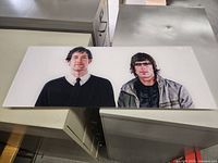 Photographic print featuring two men in black and gray clothing on a flat rigid surface with some wear.