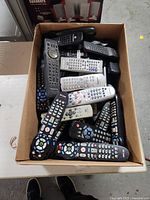 Top-down view of cardboard box filled with assorted remote controls in various colors