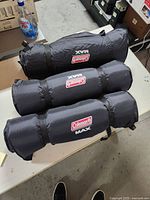 Three black Coleman Max inflatable bedrolls rolled and laid on a table, clearly labeled with brand and series.