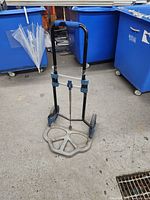 Front view of collapsible hand truck showing foldable base, black frame with blue joints, and cushioned handle grip.