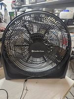 Front view of the black Comfort Zone standing fan, showcasing the center branded grille and fan blades behind the grille.