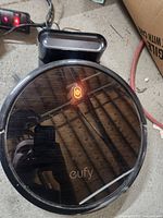 Top view of Eufy RoboVac 11S powered on with power button illuminated, showing reflective black top and Eufy logo