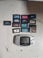 Top view of Game Boy Advance with 12 game cartridges spread out around it on a plain surface showing cartridge labels