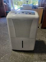Full front view of white General Electric (G.E.) dehumidifier showing front air vent and water tank slot.