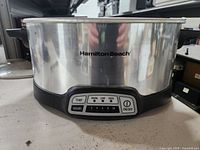 Front view of Hamilton Beach crockpot showing stainless steel body with Hamilton Beach logo and control panel with buttons.