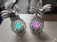 Pair of pineapple-shaped electric candle holders with color-changing electric candles lit in green, blue, and purple hues.