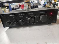 Front view of Realistic MPA-45 amplifier showing power button, master volume knob, frequency equalizer sliders, and microphone volume controls under the brand name and model.