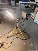Full view showing two lamps mounted on height-adjustable yellow tripod stand with one bulb lit and electrical cords visible.