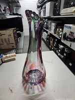 Full view of the tall hand blown glass vase on a white table.