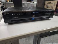 Front view of Sony multidisc DVD player showing control buttons, status display, and disc tray closed.