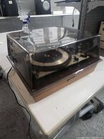 Vintage United Audio turntable with clear dust cover, wood base, and power cord visible on a table.