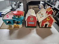Overview of all three vintage Fisher Price playsets: airport, barn, and schoolhouse arranged side by side on a table.