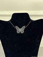Front view of black fabric choker featuring central embroidered butterfly motif displayed on stand