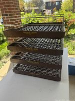 Front view of four stacked brown plastic trays with lattice base and metal side supports