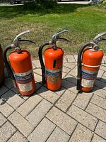 Front view of three orange fire extinguishers standing on patio