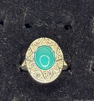 Top view of silver tone ring with oval turquoise-coloured faux stone and starburst bezel