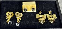 Three pairs of earrings: gold rhinestone bow drops with clear stones, silver rose studs on card, gold bow and heart drops