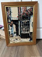 Front view of framed needlepoint artwork showing Paris storefront scene