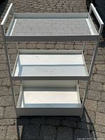 Front view of white metal utility cart showing three shelves
