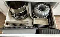 Top-down photo of a drawer filled with various baking pans including muffin tins, springform pans, Bundt pan, loaf pans, and tart pans.