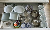 Photo showing an open kitchen drawer with a variety of ceramic and metal bowls, ramekins, and serving dishes organized inside.