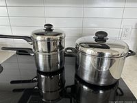 Photo showing stainless steel stock pot with lid and smaller steamer pot with lid stacked inside on a stovetop.