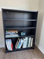 Black IKEA bookcase against wall containing books for scale only, bookcase sold empty