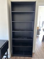 Photo of a tall, dark wood colored IKEA bookcase with five shelves against a neutral wall.