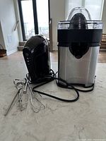 KitchenAid hand mixer in black with two metal beaters, and Cuisinart stainless steel citrus juicer with black and transparent parts on a countertop.