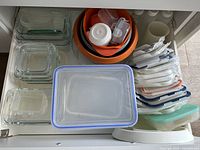 Drawer shelf with multi-sized glass and plastic kitchen storage containers stacked neatly including orange and white plastic bowls