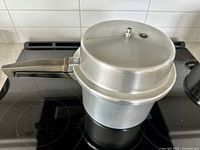 Silver Prestige pressure cooker on black stovetop with white tiled backsplash.