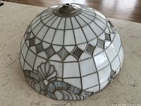 Dome-shaped Tiffany style stained glass pendant light shade in white and gray glass with leaded framework, resting on flat surface showing intricate glass and metalwork detail.