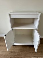 Front view of white melamine storage cart with open double doors showing interior storage space.