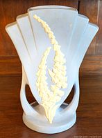 Front and angled view of Art Deco style ceramic vase with light gray finish and yellow floral relief on wooden surface.