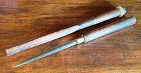 Antique cutting utensil with blade and wooden sheath laid on wooden surface.