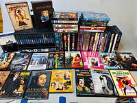 Overview of large collection of DVDs, Blu-Rays, and VHS showing boxsets including Indiana Jones and Back to the Future and multiple individual movie titles spread out on a table.