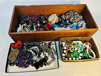 Overview of three containers filled with assorted jewelry including necklaces, bracelets, and earrings with various bead designs and colors.
