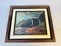 Framed print showing Lawren Harris's The Ice House featuring a landscape with hills, water, and a prominent ice house building under a cloudy sky, enclosed in wooden frame with white and gold matting.
