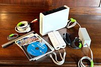 Full lot showing Nintendo Wii console, cables, controllers, and game cases arranged on a wooden surface.