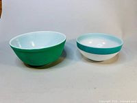 Two vintage blue-green glass mixing bowls shown side by side; one bowl is matte finish blue-green and larger, the other is glossy blue-green and white with a band design and smaller size.