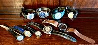 Photo showing collection of 10 assorted Timex watches on a wooden surface, featuring men's and ladies styles with various strap types and dial colors.